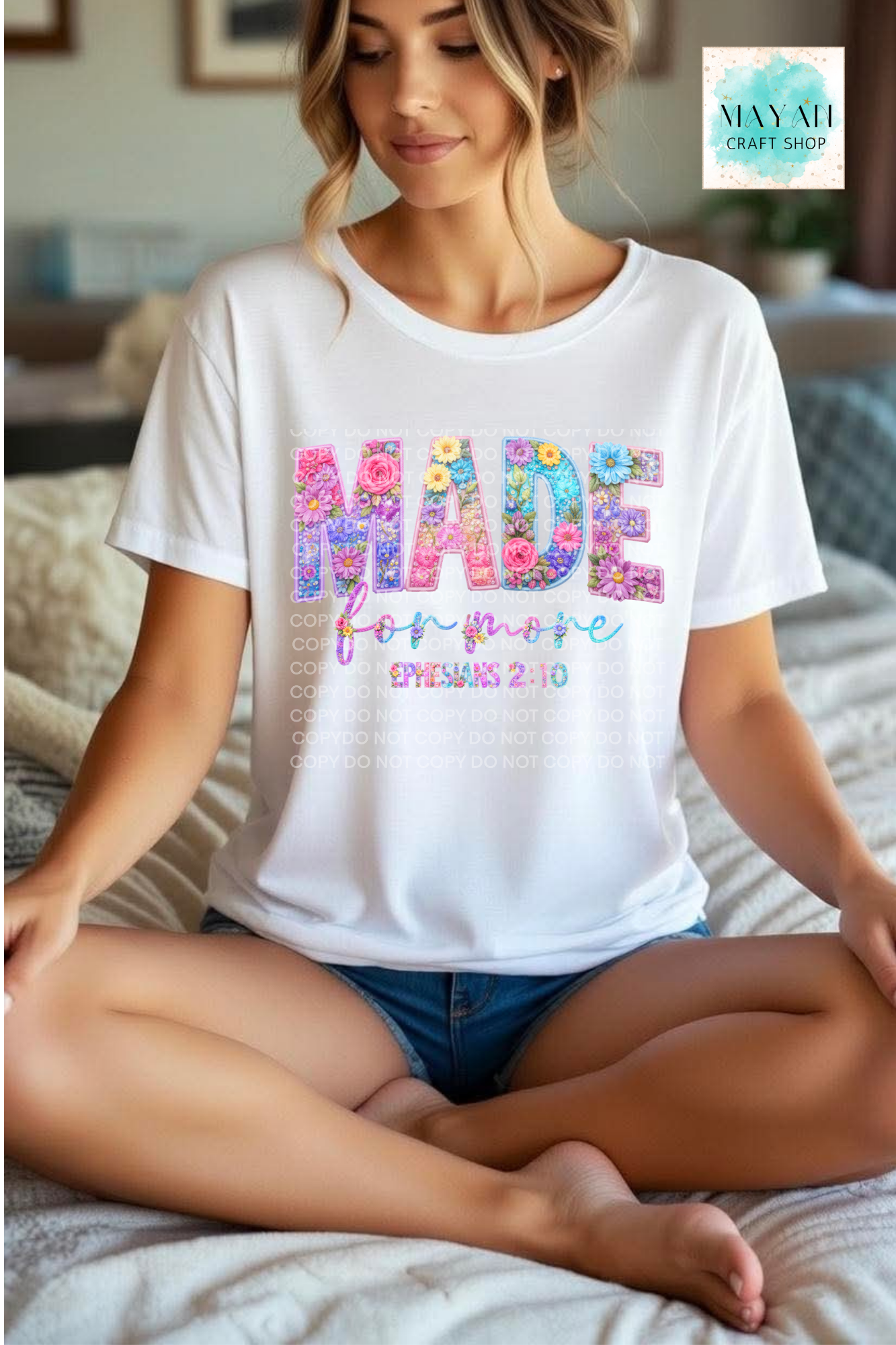 Woman wearing a white t-shirt with colorful text sitting on a bed.