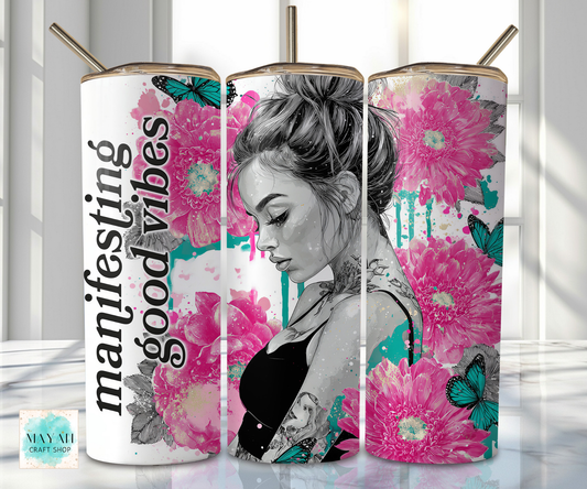 Tumbler with a design of a woman with flowers and text 'manifesting good vibes' on a white background.