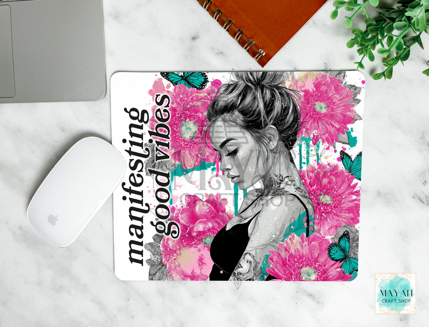 Mouse pad with a design of a woman and flowers, text 'manifesting good vibes', on a marble surface.