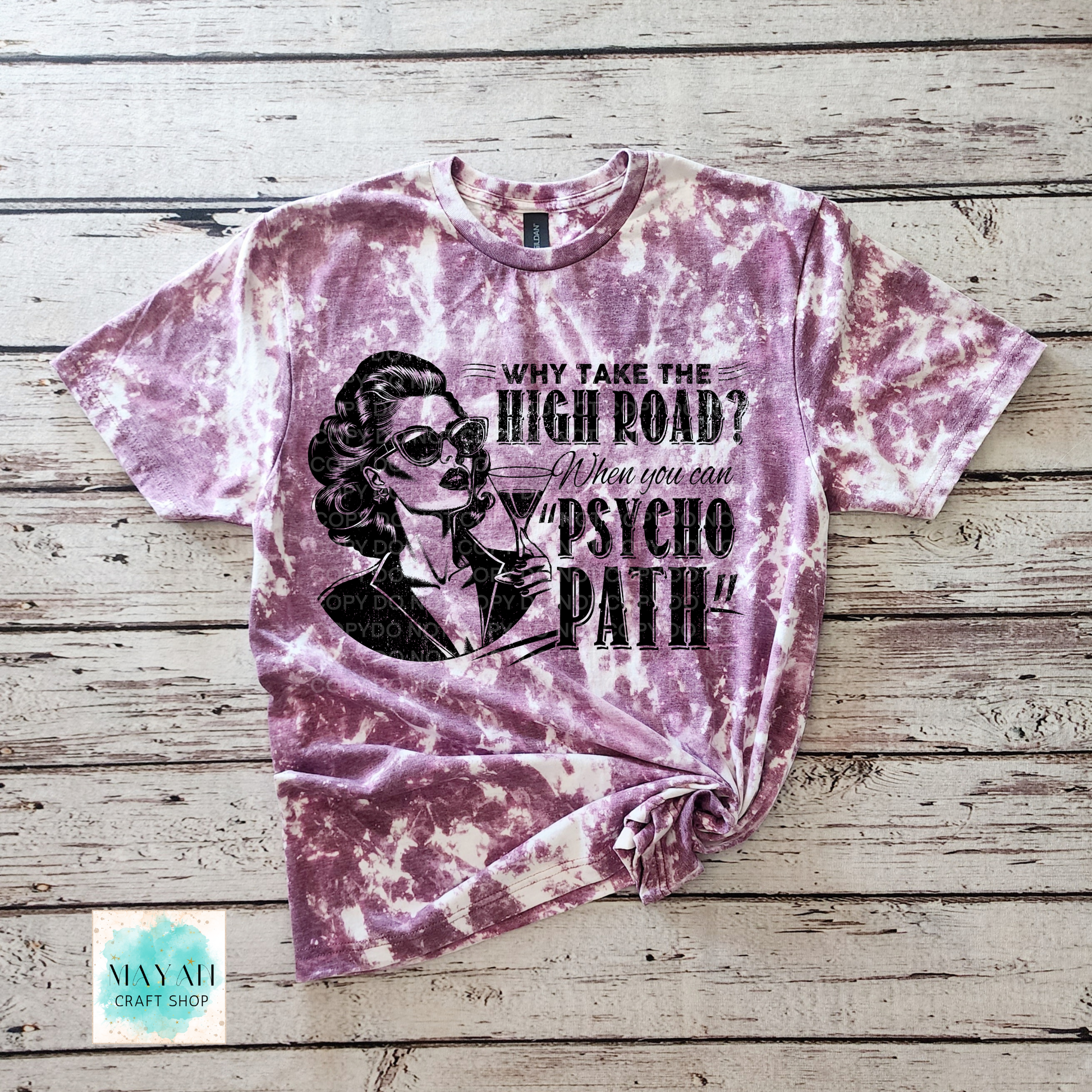 Tie-dye t-shirt with graphic design and text on a wooden surface, featuring the brand 'Mayan Craft Shop'.