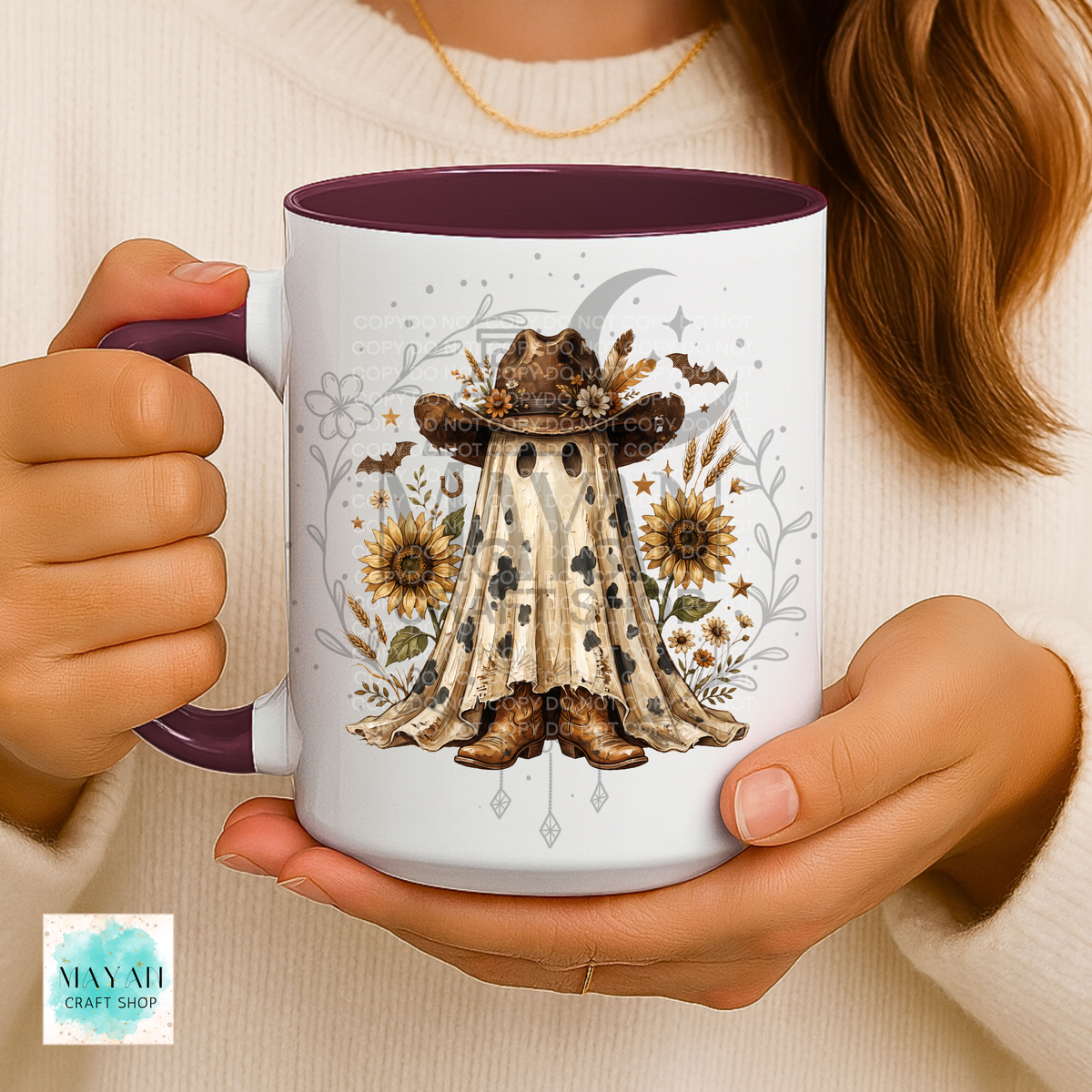 A person holds a white ceramic mug with a dark purple interior and handle. The mug features a detailed graphic of a witch in a hat and cape surrounded by sunflowers, bats, and a crescent moon.