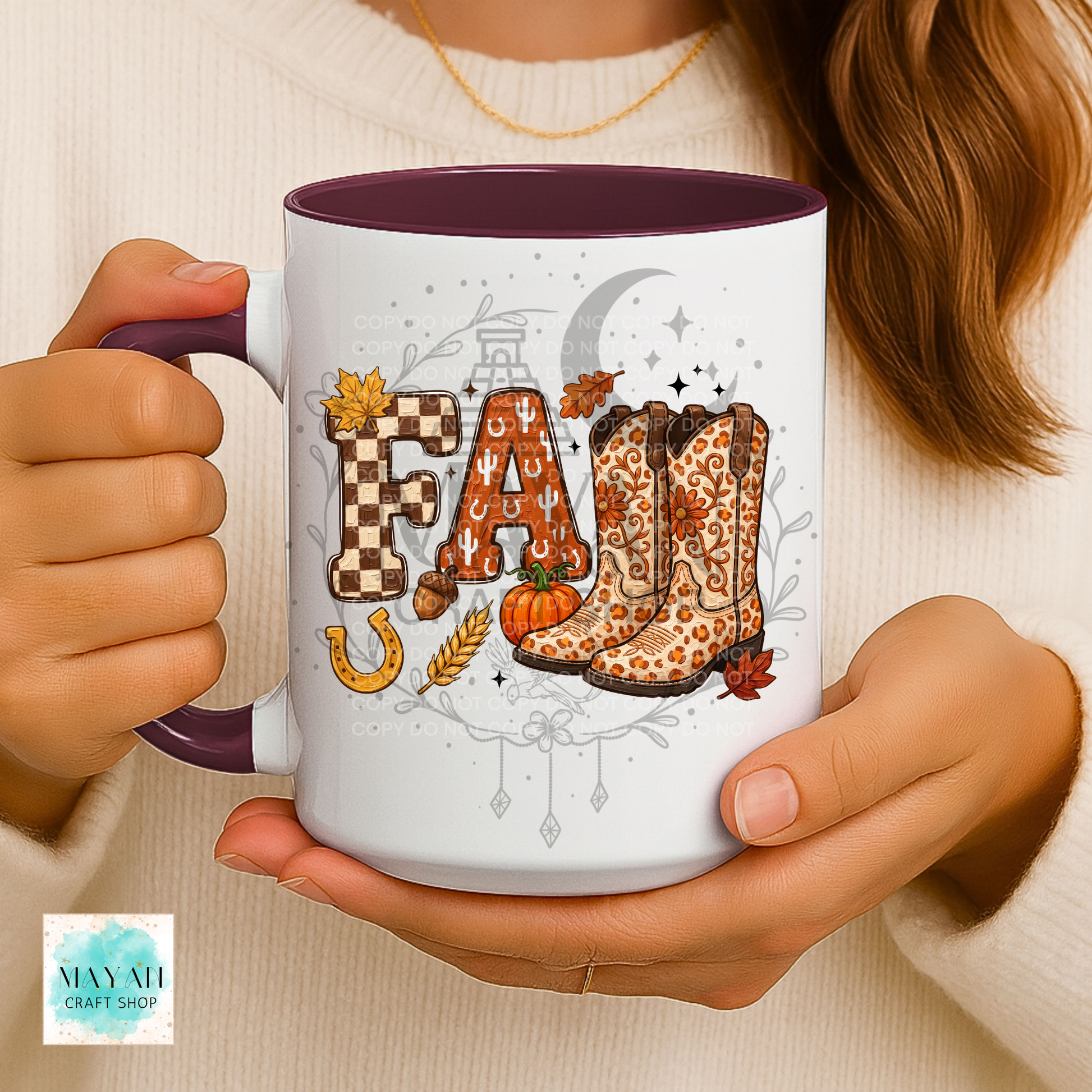 A person holds a white ceramic mug with a dark purple interior and handle. The mug features a fall-themed graphic with the word 'FALL' in leopard-print cowboy boots, checkered letters, a pumpkin, wheat, a horseshoe, and autumn leaves.
