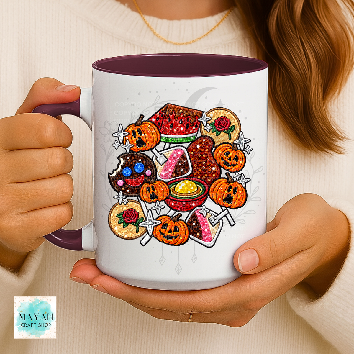 A person holds a white ceramic mug with a maroon handle and interior. The mug is decorated with a colorful Halloween-themed graphic featuring mexican candy.