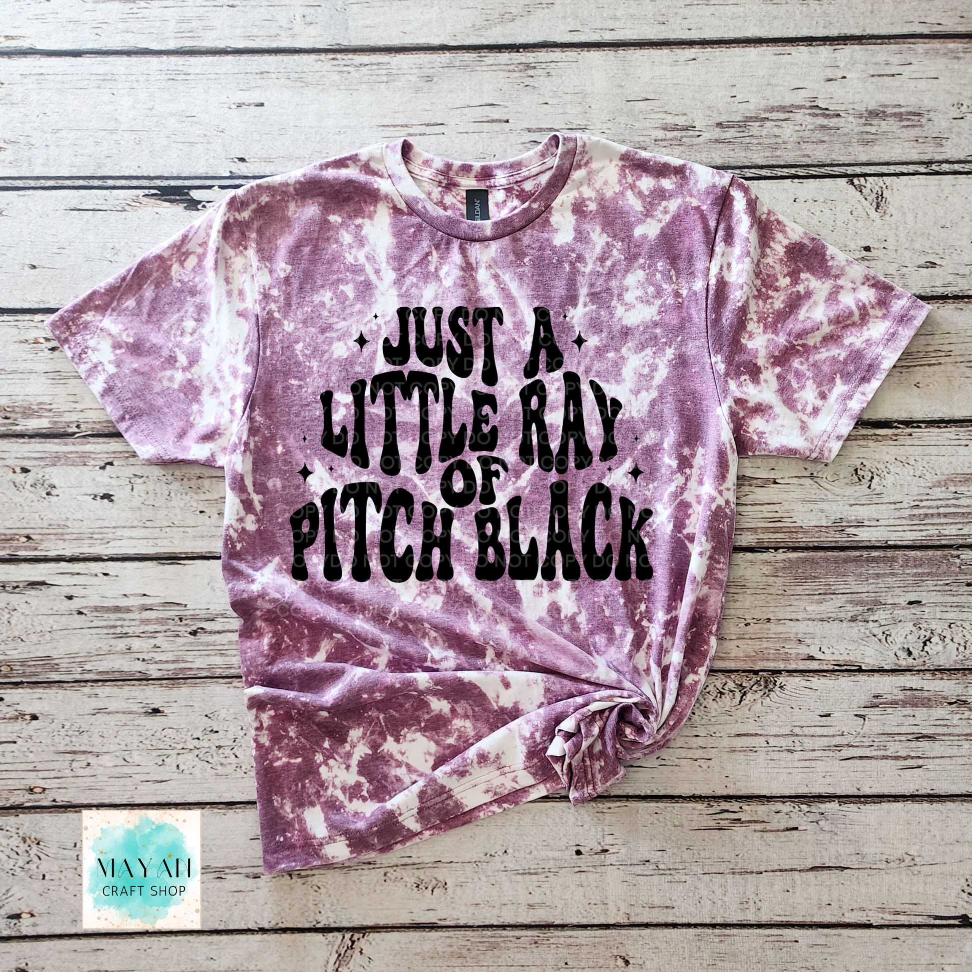 Tie-dye t-shirt with text on a wooden surface, featuring the brand 'Mayan Craft Shop'.