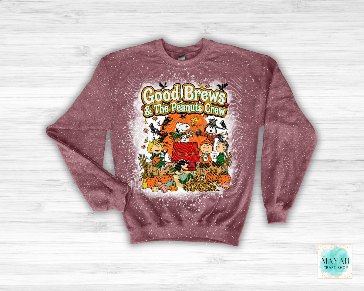 A heathered maroon crewneck sweatshirt featuring a colorful graphic of the 'Good Brews' in a pumpkin-themed setting, displayed flat on a white wood background.