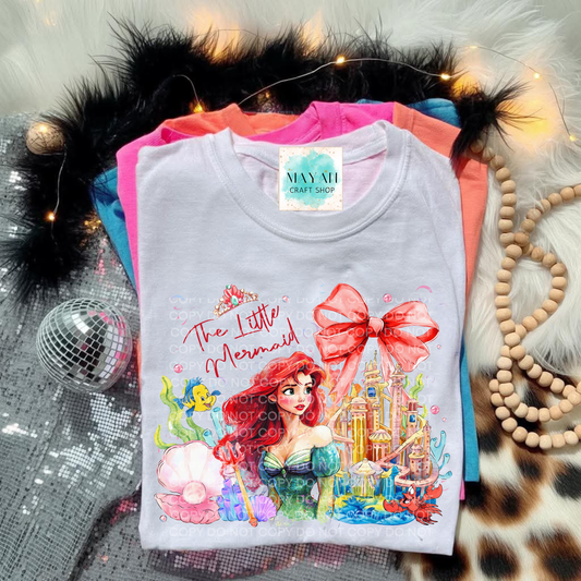 T-shirt with a mermaid design on a textured surface with decorative items.