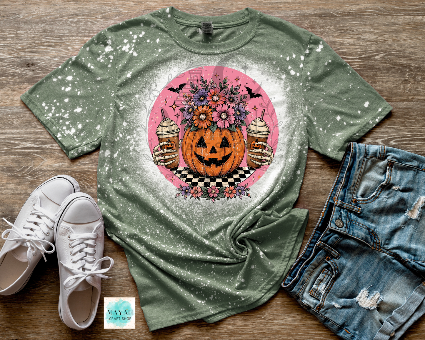 Green t-shirt with Halloween design on a wooden surface with white sneakers and denim shorts.