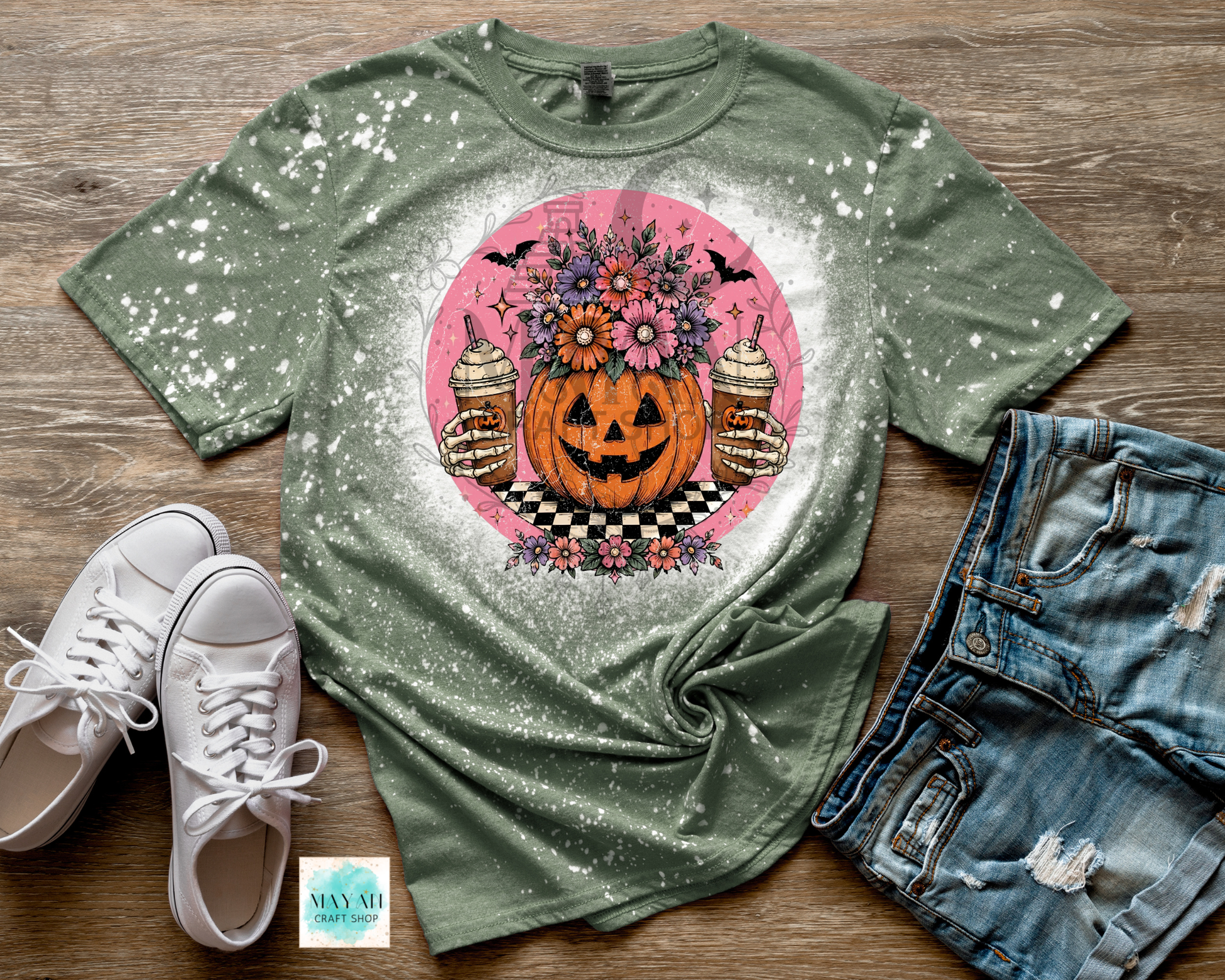 Green t-shirt with Halloween design on a wooden surface with white sneakers and denim shorts.