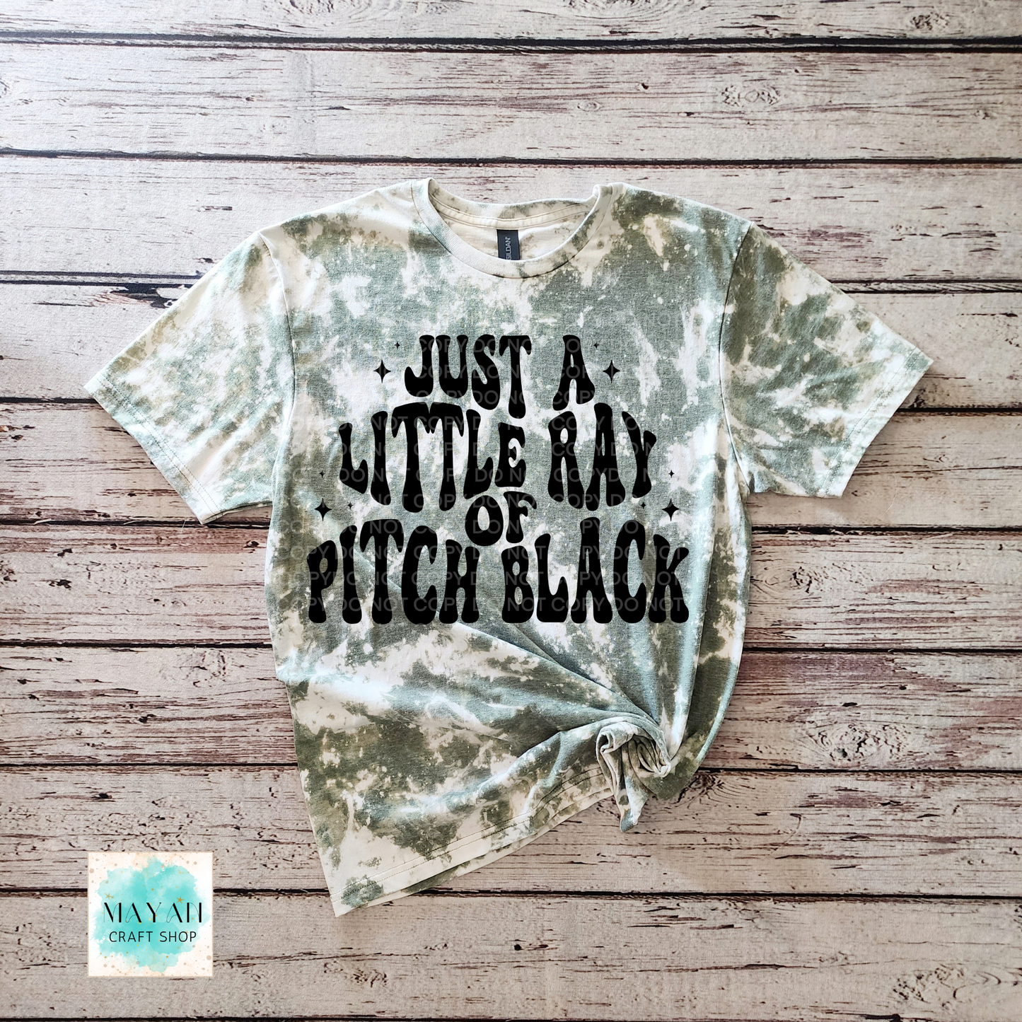Tie-dye t-shirt with text on a wooden surface, featuring the brand 'Mayan Craft Shop'.