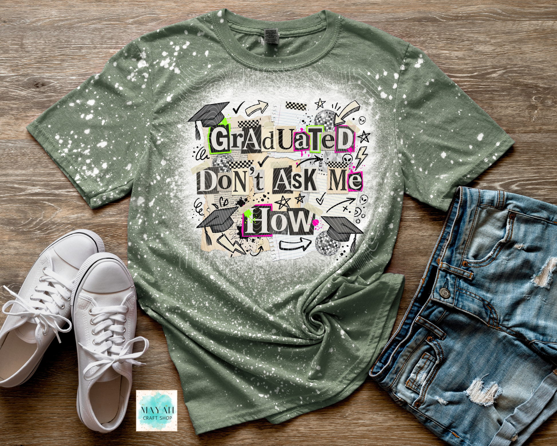 Green bleached t-shirt with graduation design, white sneakers, and denim shorts on a wooden surface.