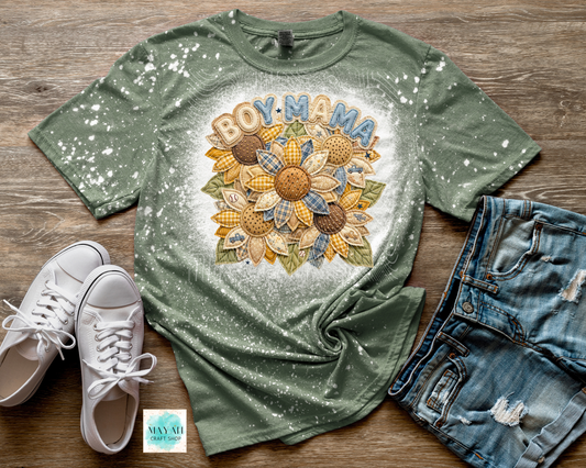 Green t-shirt with 'BOY MAMA' and sunflower design on a wooden surface with white sneakers and denim shorts.