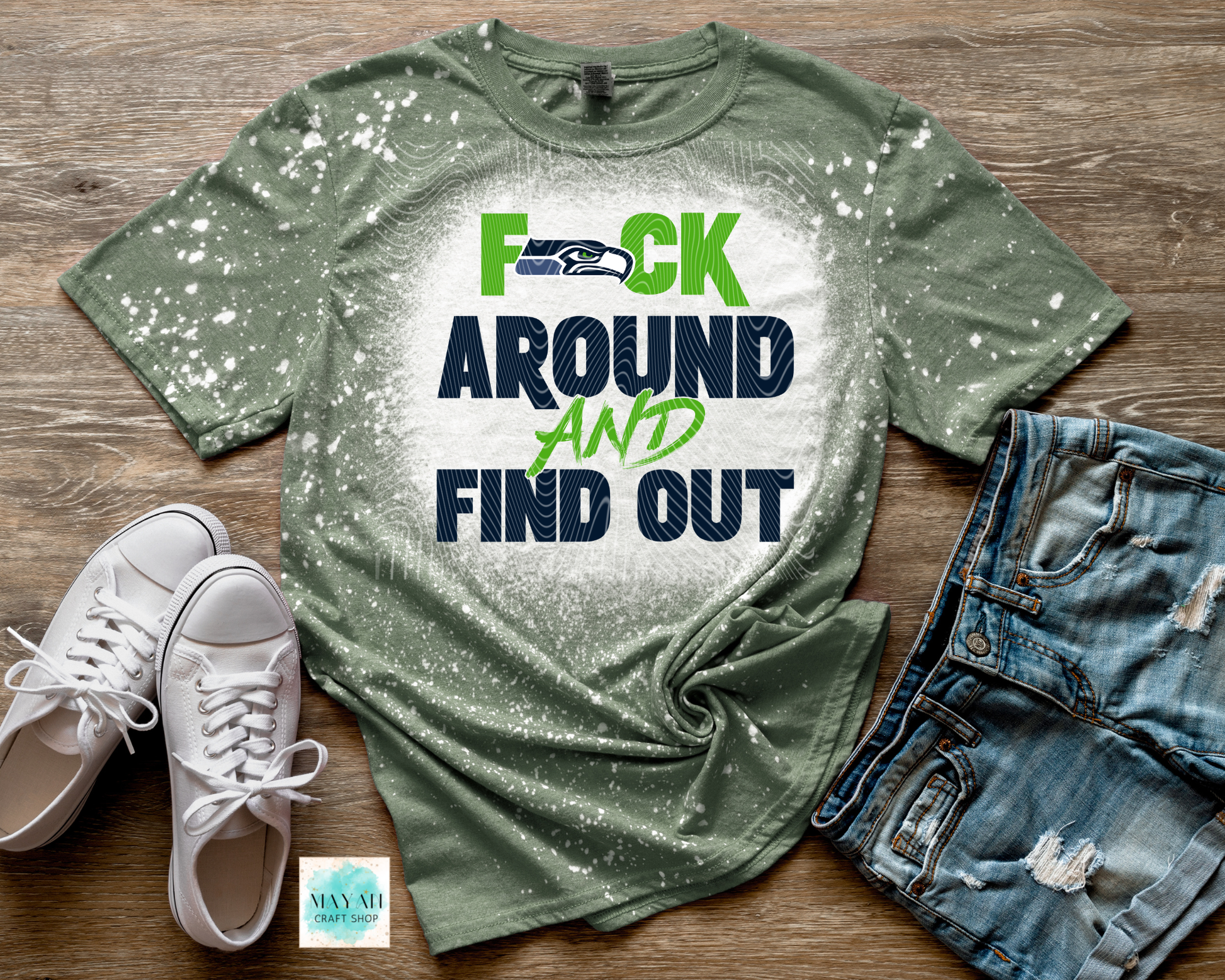 Green t-shirt with graphic design on a wooden surface with shoes and shorts.