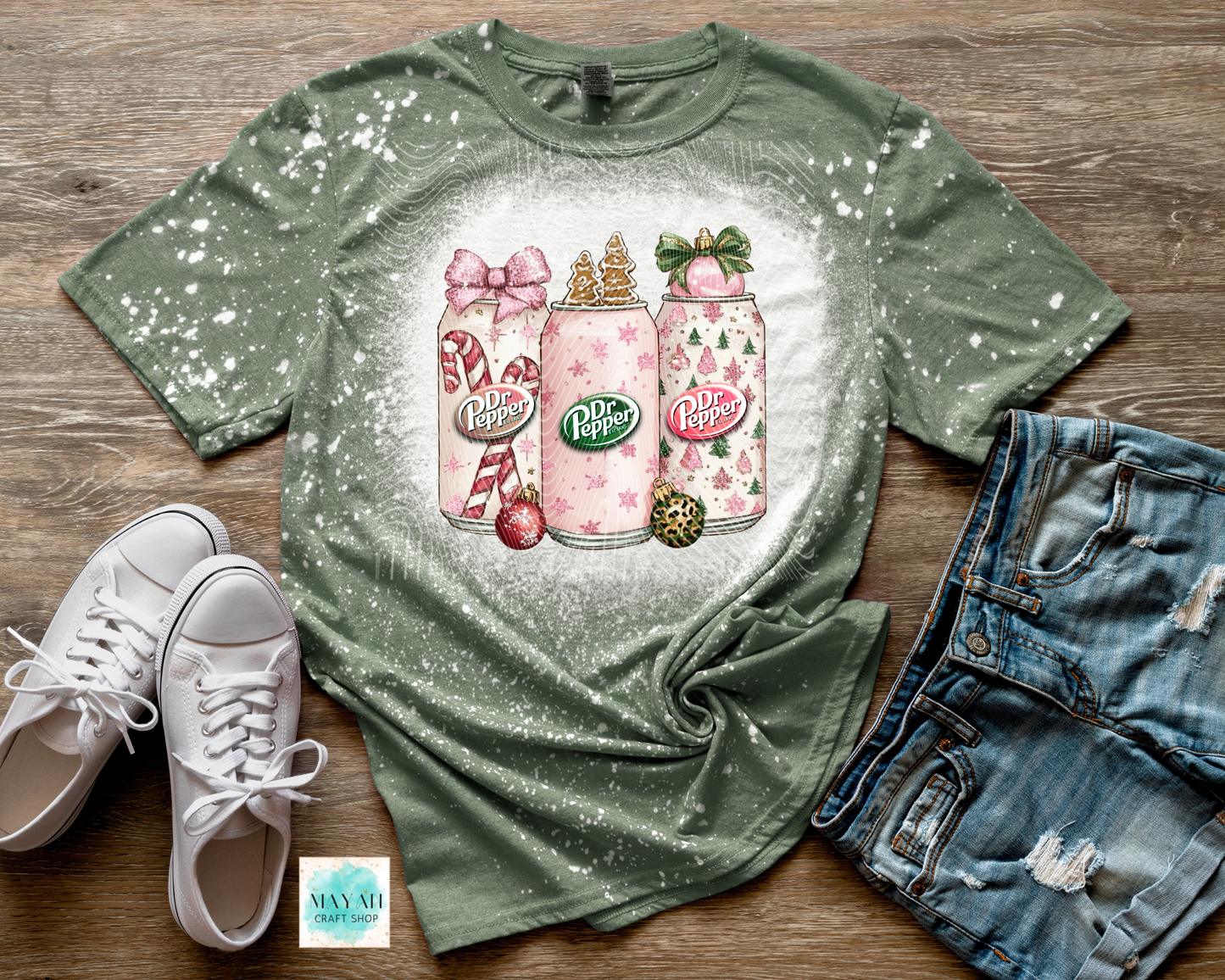 Green t-shirt with pink soft drinks bottles design on a wooden surface with white sneakers and denim shorts.