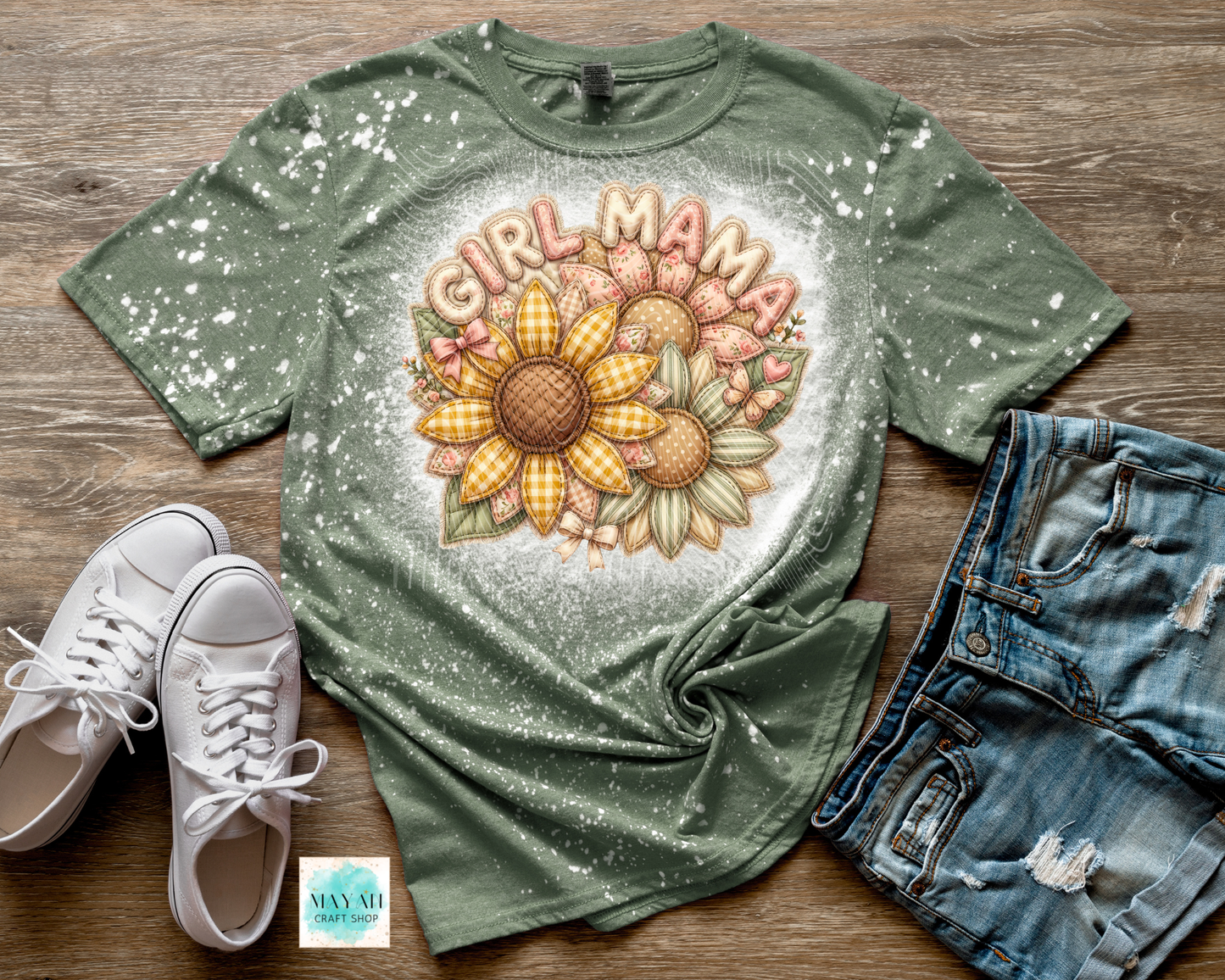 Green t-shirt with 'Girl Mama' and sunflower design on a wooden surface with white sneakers and denim shorts.