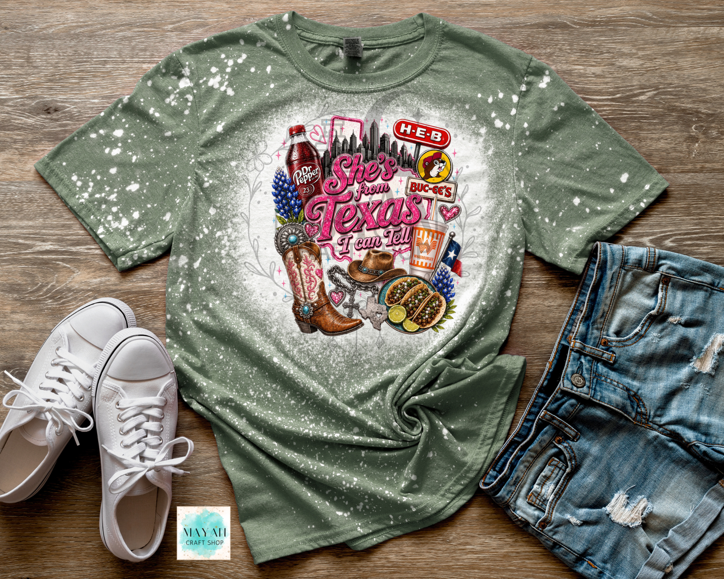 Green t-shirt with Texas-themed design on a wooden surface with white sneakers and denim shorts.