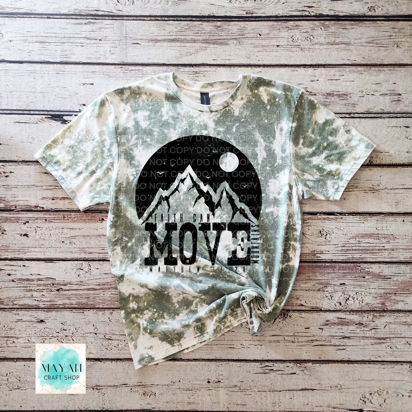 Dye-sublimated t-shirt with mountain design and 'MOVE' text on a wooden surface, featuring the brand 'Mayah Craft Shop'.