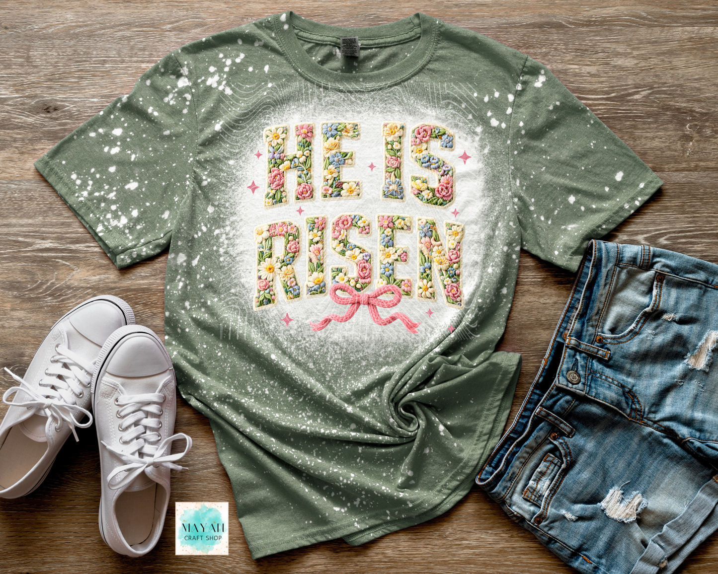 Green t-shirt with floral text design, white sneakers, and denim shorts on a wooden surface.