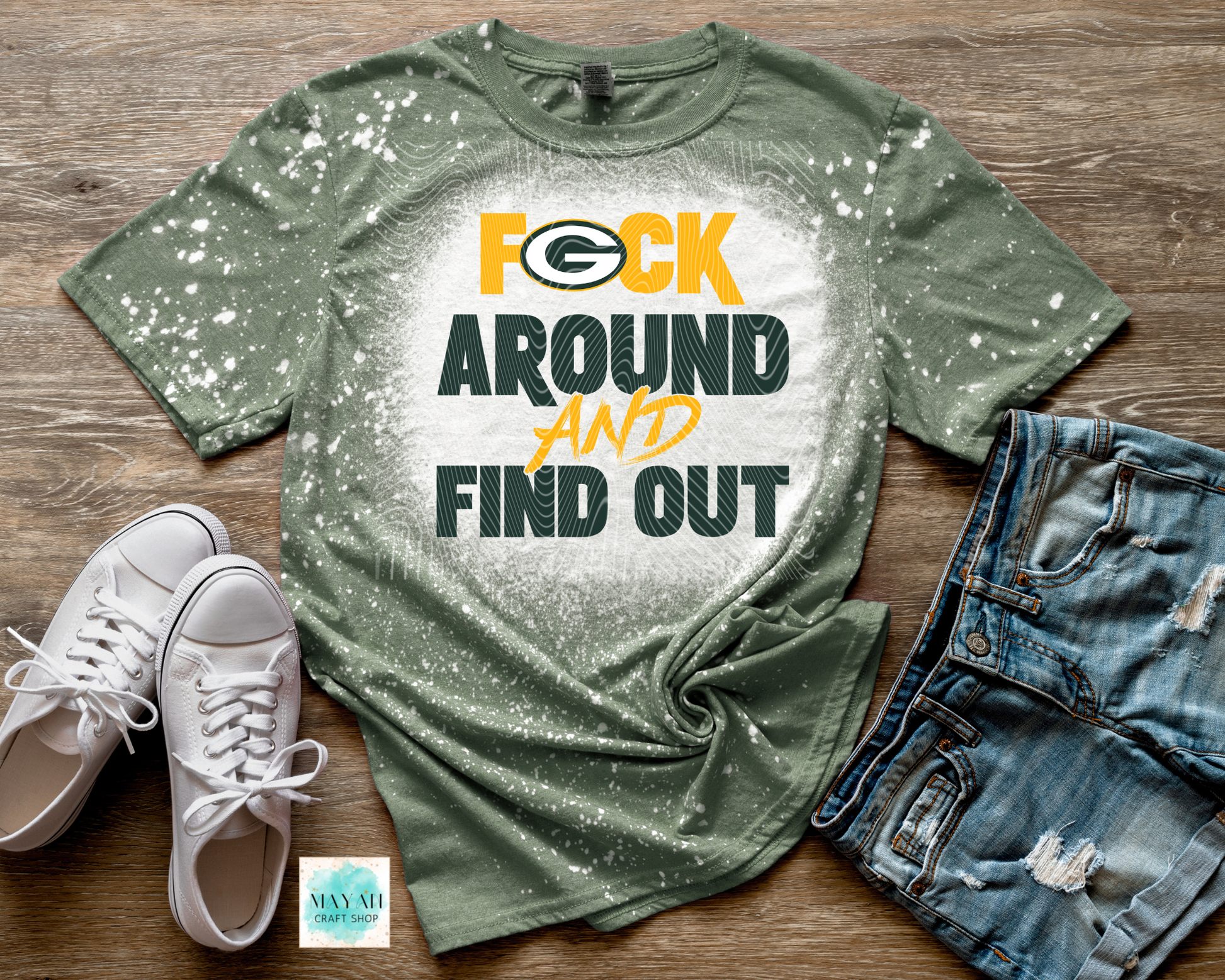 Green t-shirt with graphic text, white sneakers, and denim shorts on a wooden surface