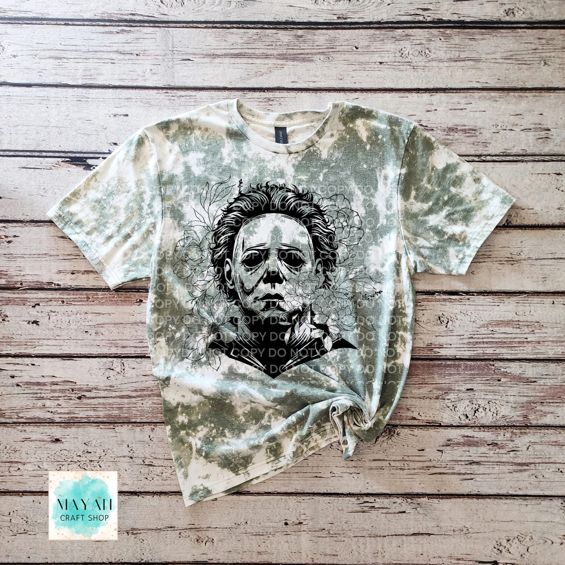 T-shirt with graphic design on a wooden surface, featuring a brand logo in the corner.