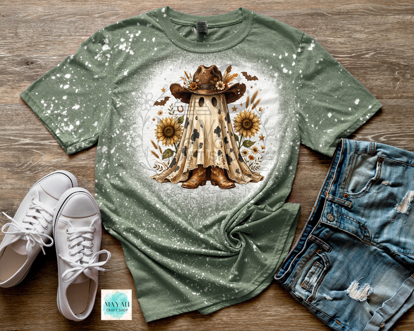A heather military green splatter-dyed graphic t-shirt featuring a central illustration of a cowboy in a hat and boots surrounded by sunflowers, styled in a flat lay with white sneakers, distressed denim shorts.