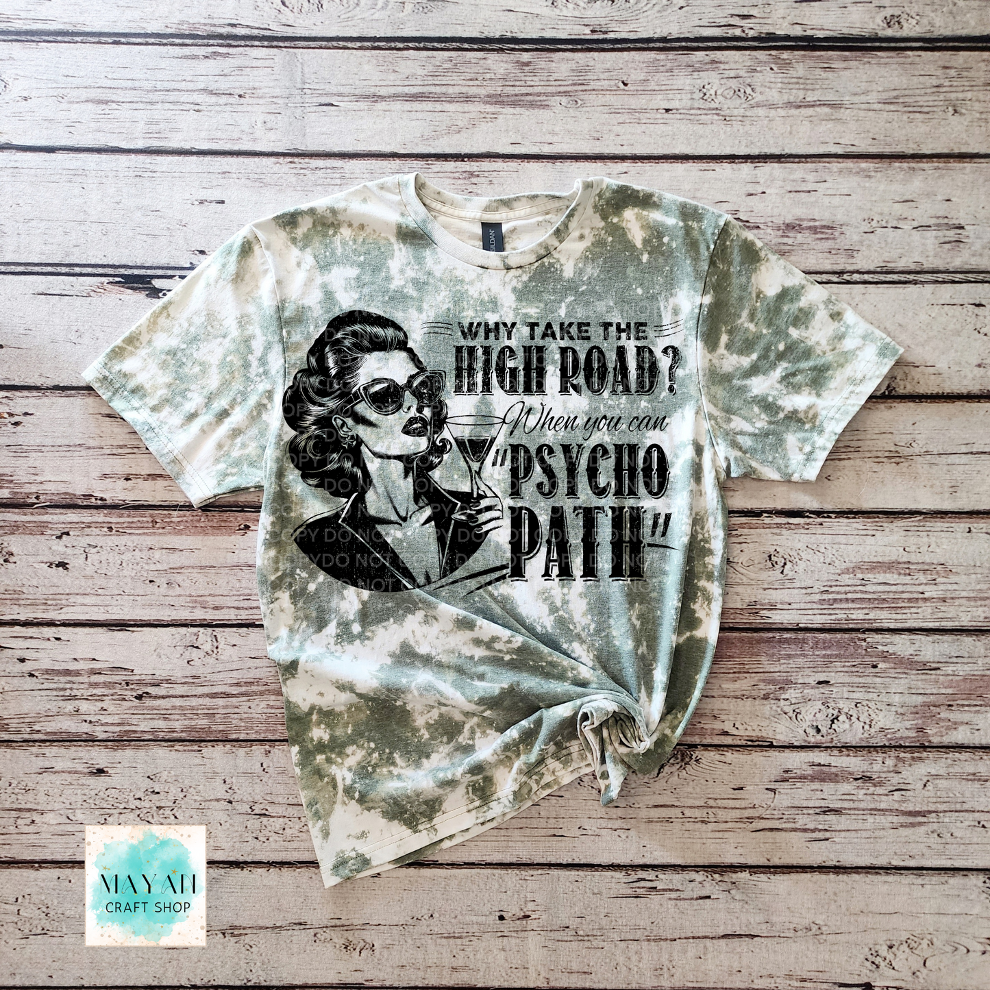 T-shirt with graphic design and text on a wooden surface, featuring a brand logo in the corner.