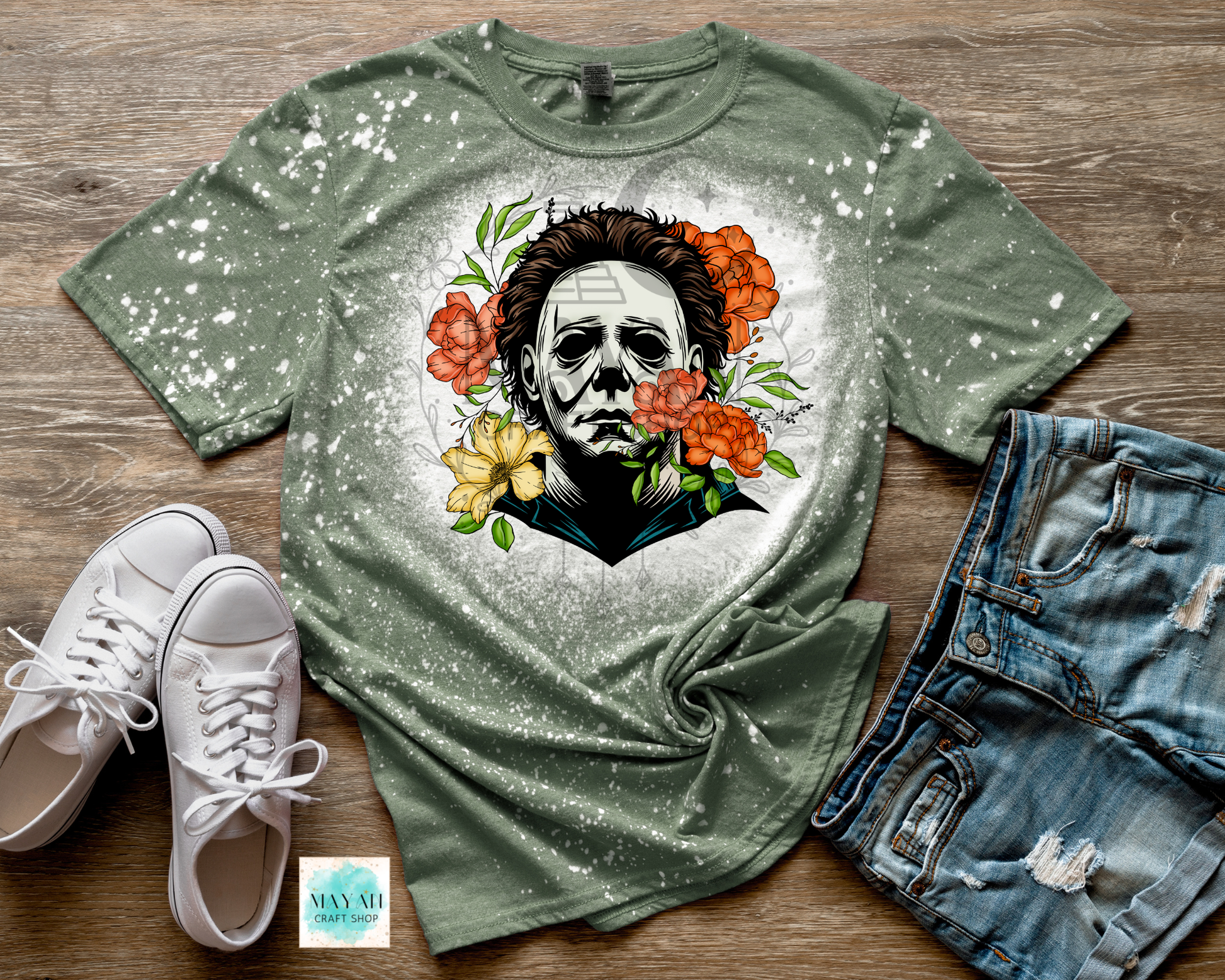 Green t-shirt with a graphic design of a face surrounded by flowers, paired with white sneakers and denim shorts on a wooden surface.