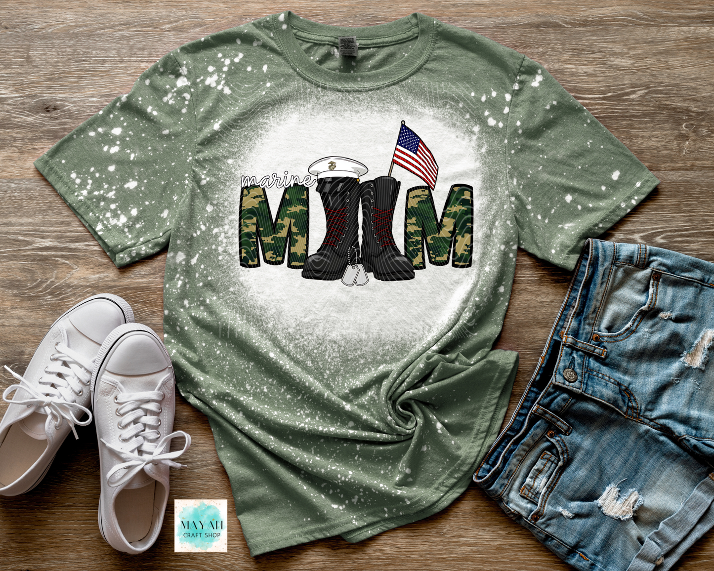 Green t-shirt with military-themed design on a wooden surface with shoes and shorts.