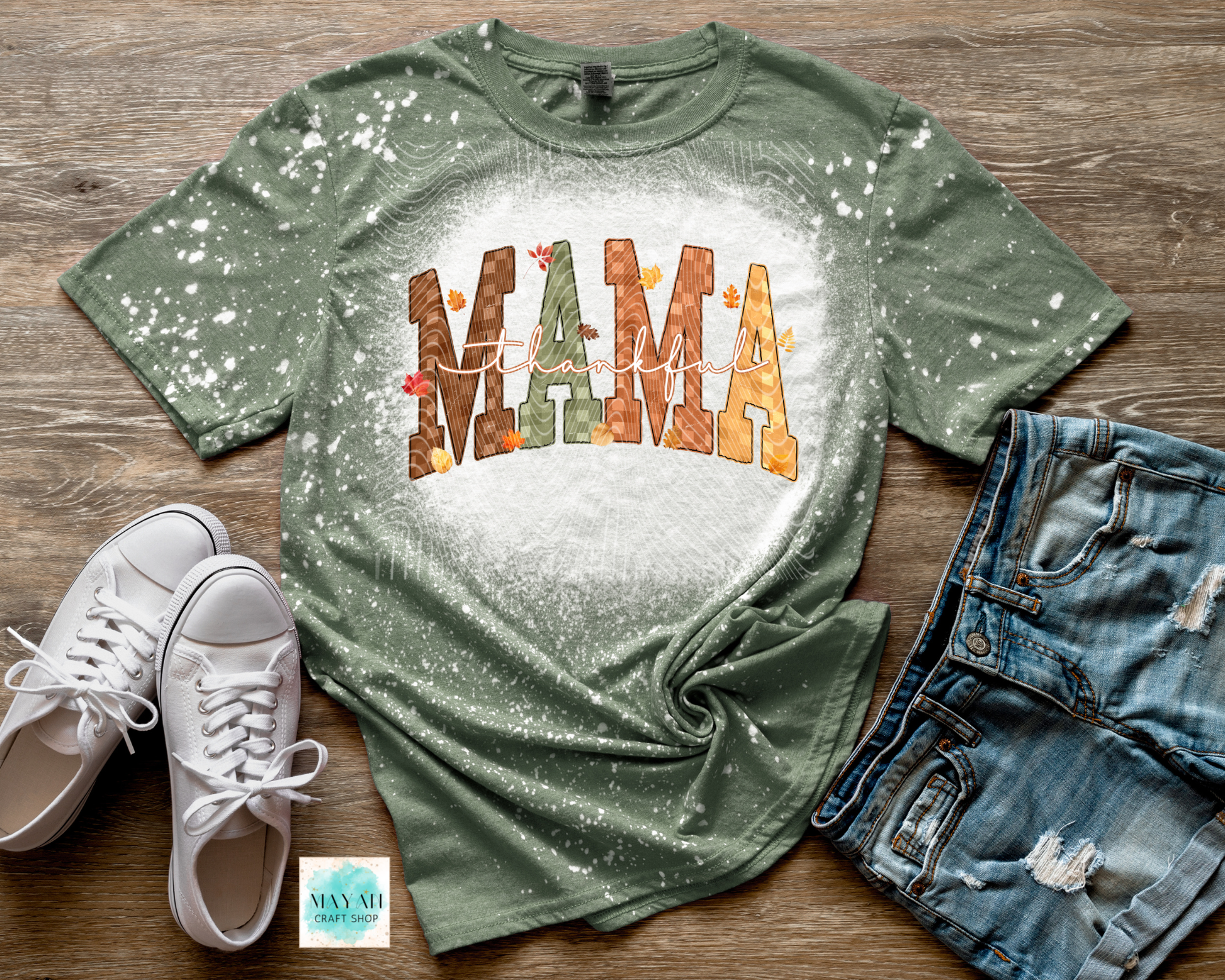 Green t-shirt with 'MAMA' text on a wooden surface with shoes and shorts.