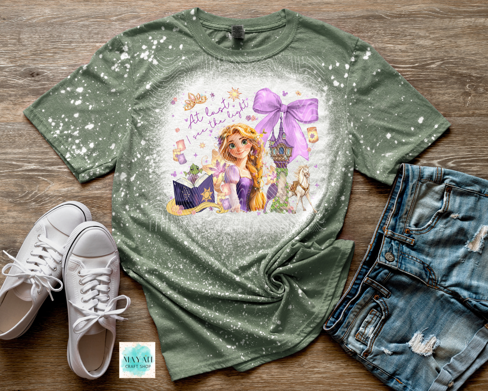 Green t-shirt with princess design on a wooden surface with shoes and shorts.