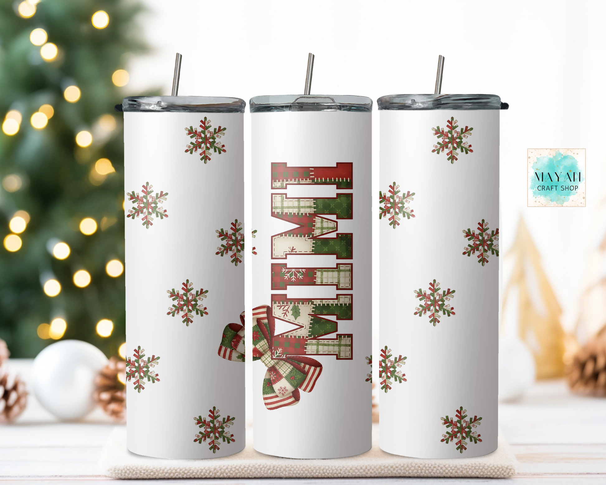 Three white tumblers with Christmas-themed designs on a surface with a blurred festive background.