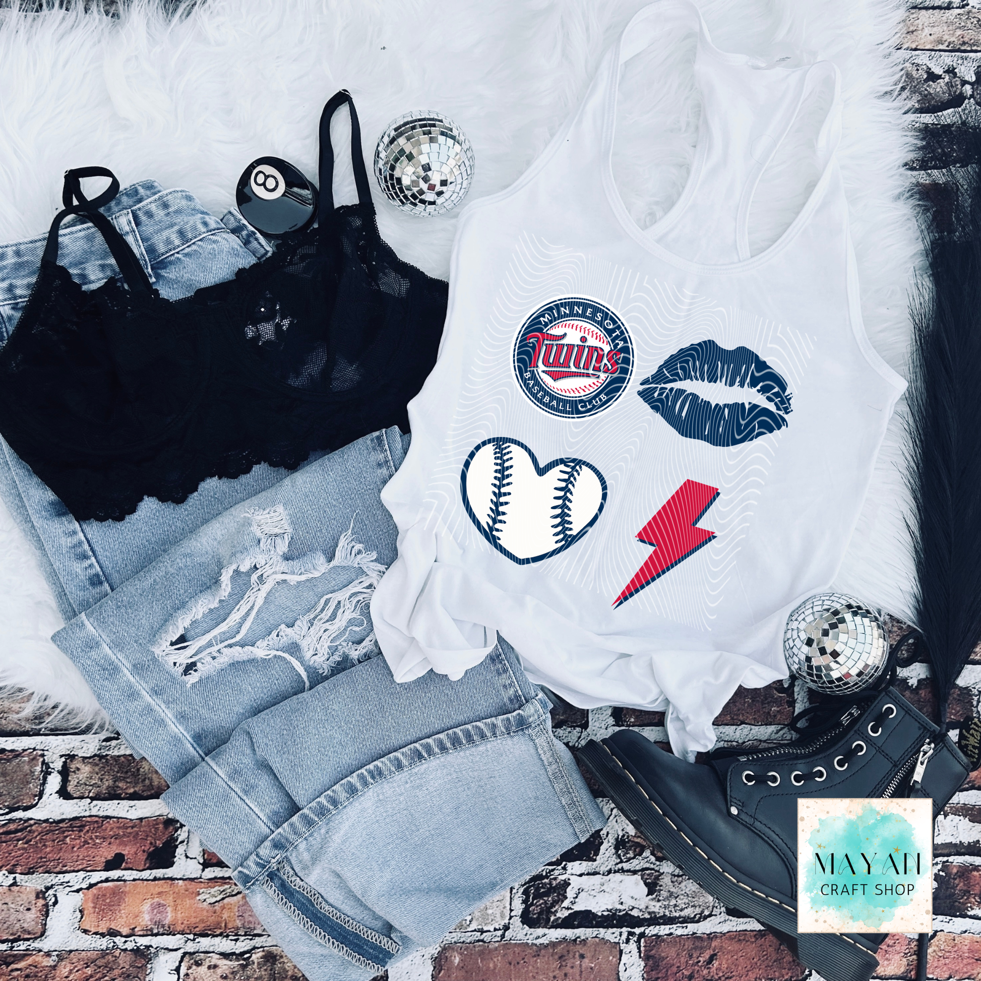 White tank top with sports-themed designs on a brick surface, surrounded by denim shorts and black lace top.