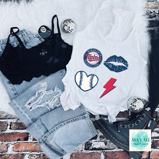 White tank top with sports-themed designs on a brick surface, surrounded by denim shorts and black lace top.