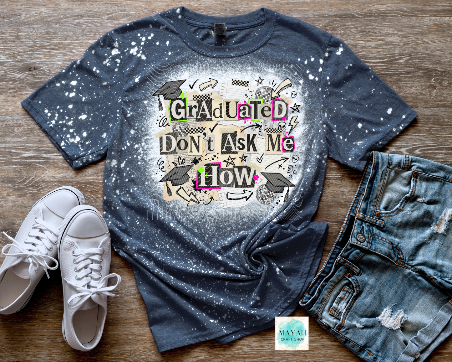 Blue splatter t-shirt with graduation design, white sneakers, and jeans on a wooden surface