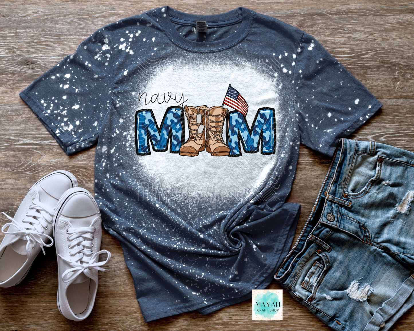 Blue splatter t-shirt with military mom text, boots, and American flag on a wooden surface with white sneakers and jeans.