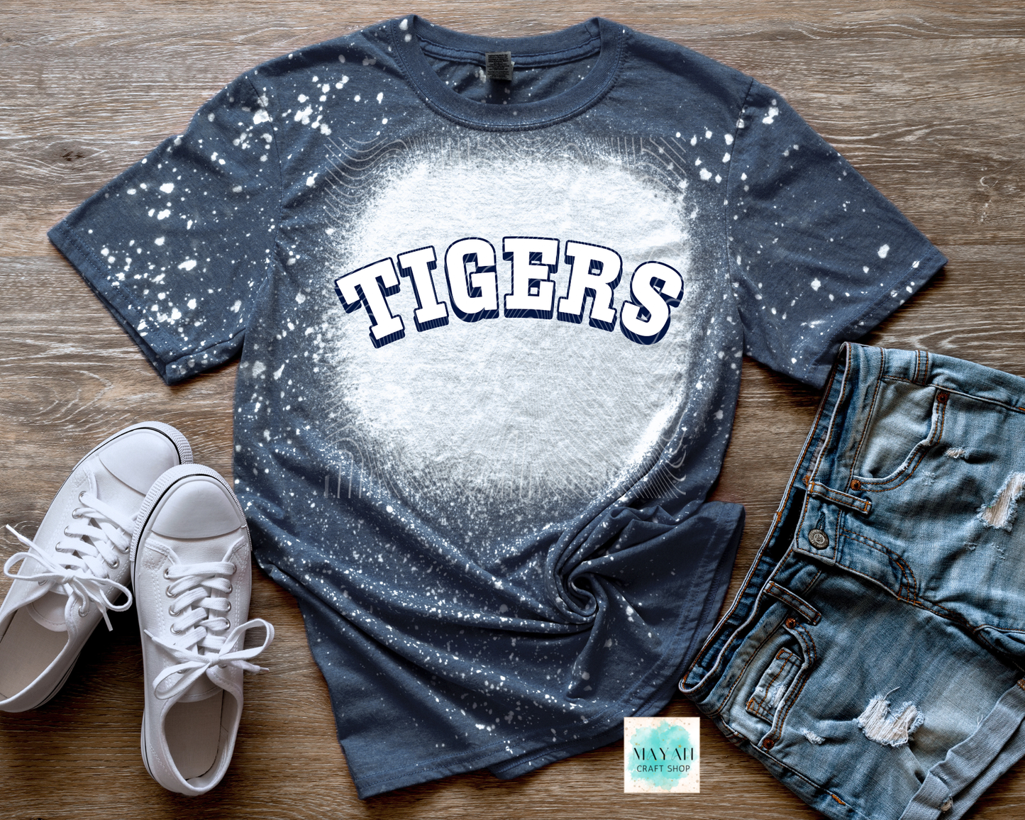 Bleached t-shirt with 'TIGERS' text, white sneakers, and denim shorts on a wooden surface.
