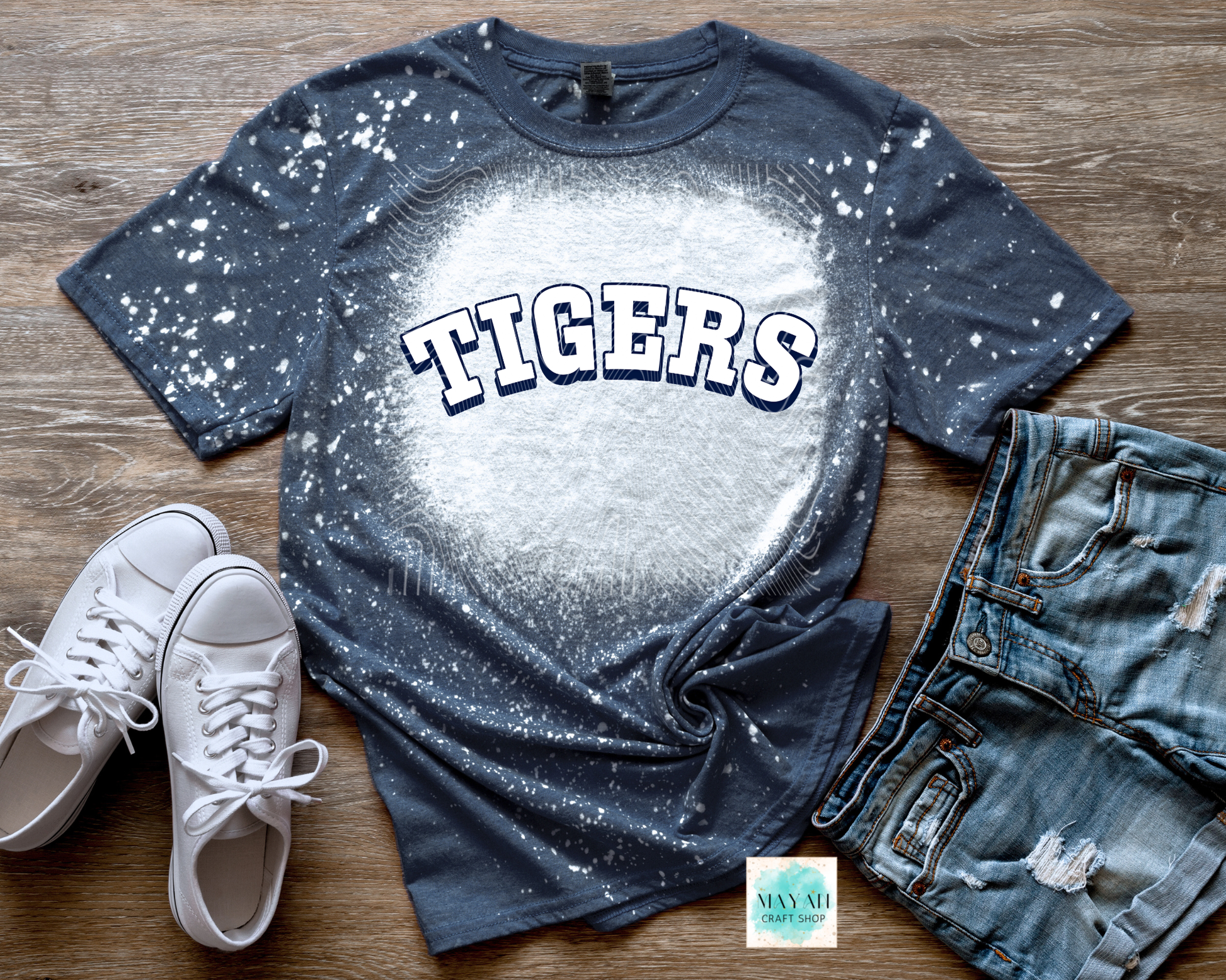 Bleached t-shirt with 'TIGERS' text, white sneakers, and denim shorts on a wooden surface.