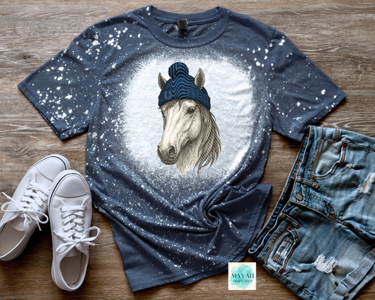 Blue t-shirt with horse graphic, white sneakers, and jeans on a wooden surface