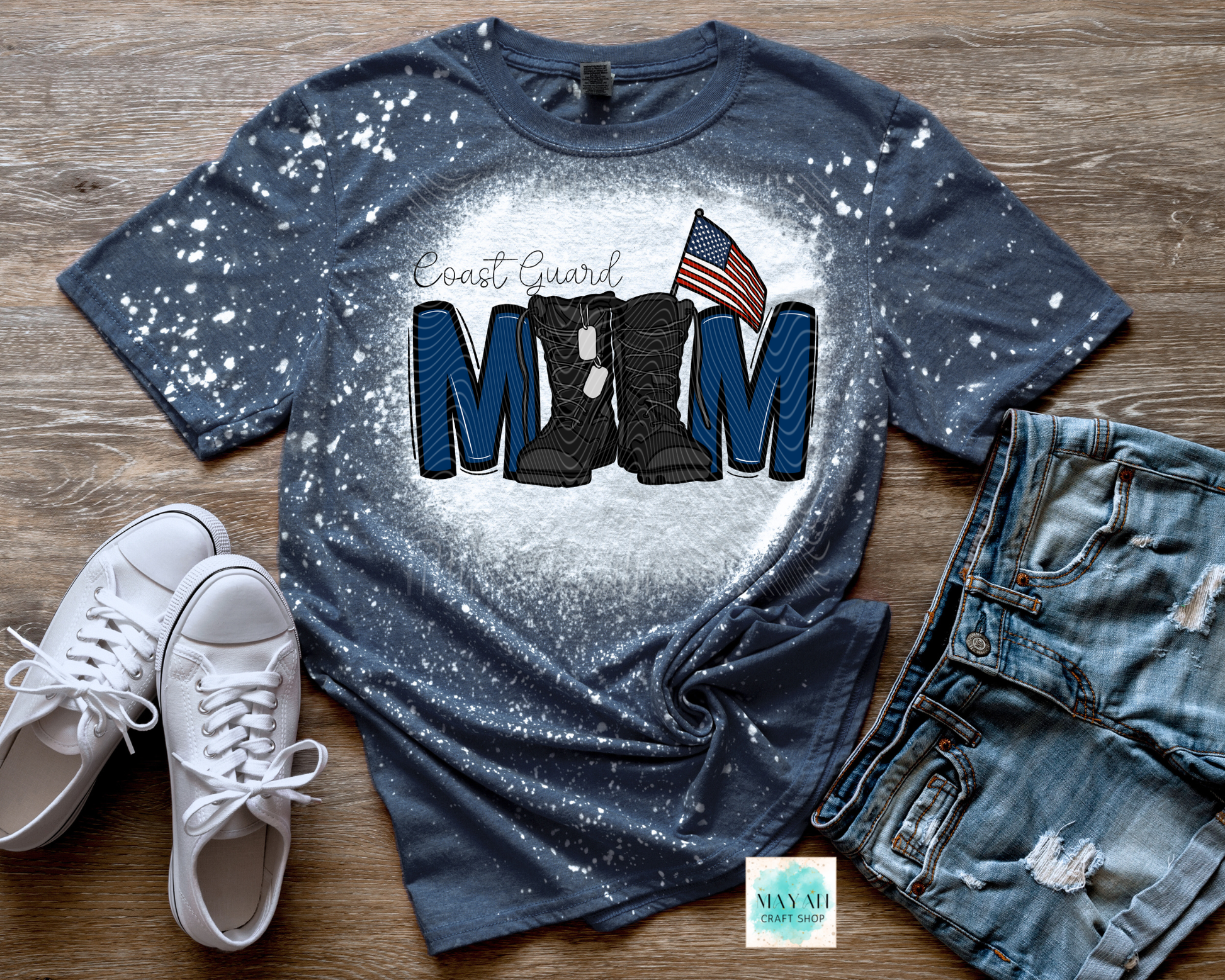 Blue splatter paint t-shirt with military mom text, boots, and American flag on a wooden surface with white sneakers and jeans.
