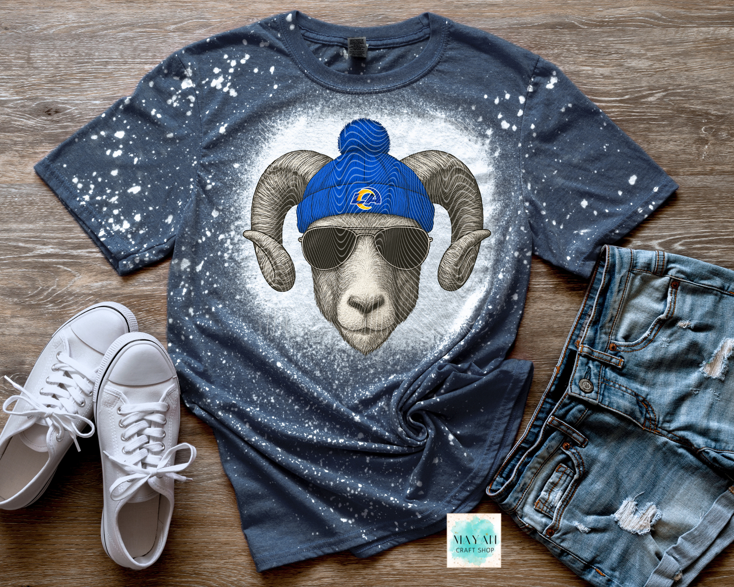 T-shirt with a graphic of a ram wearing sunglasses and a blue beanie, paired with white sneakers and jeans on a wooden surface.