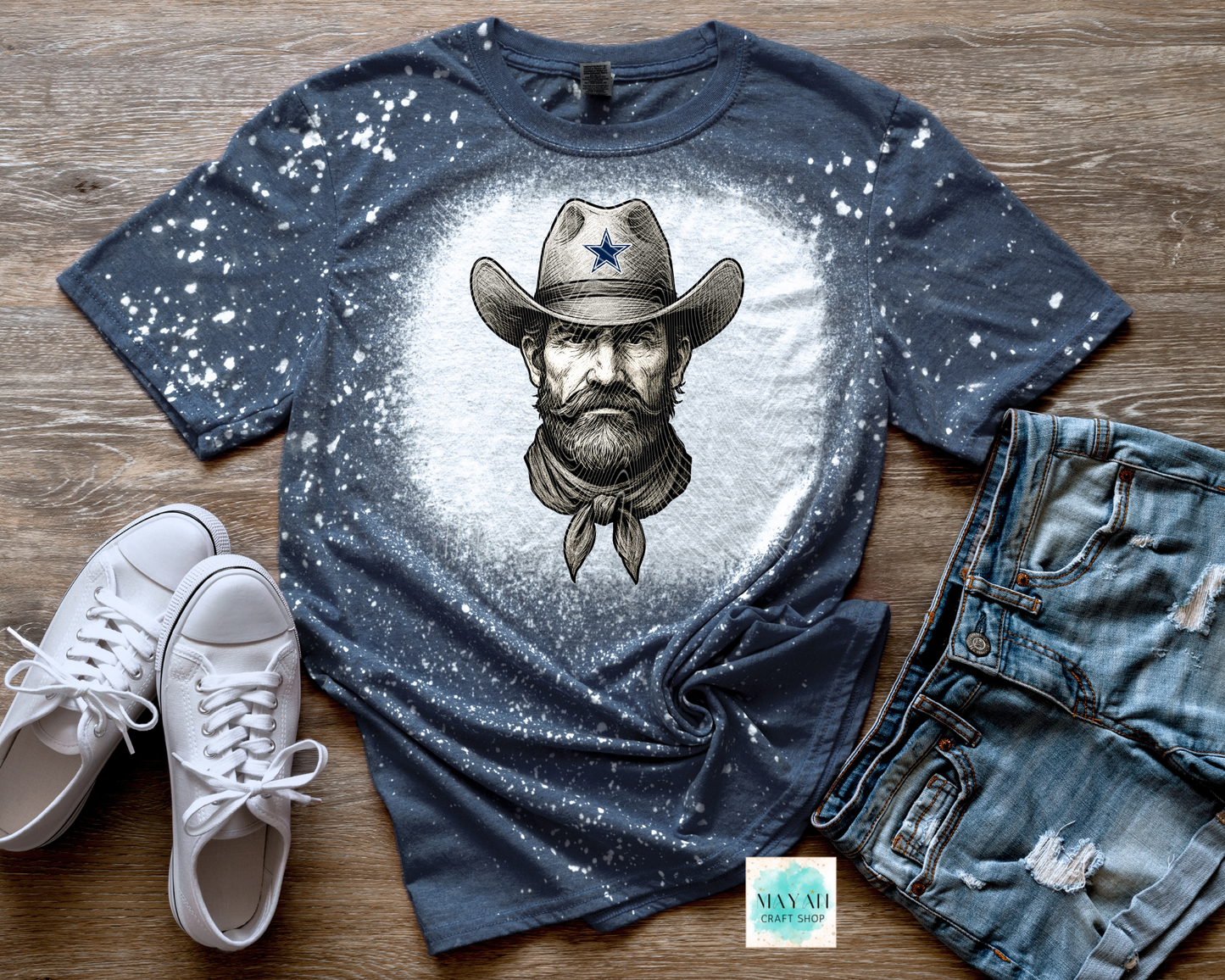Blue t-shirt with cowboy graphic, white sneakers, and jeans on a wooden surface
