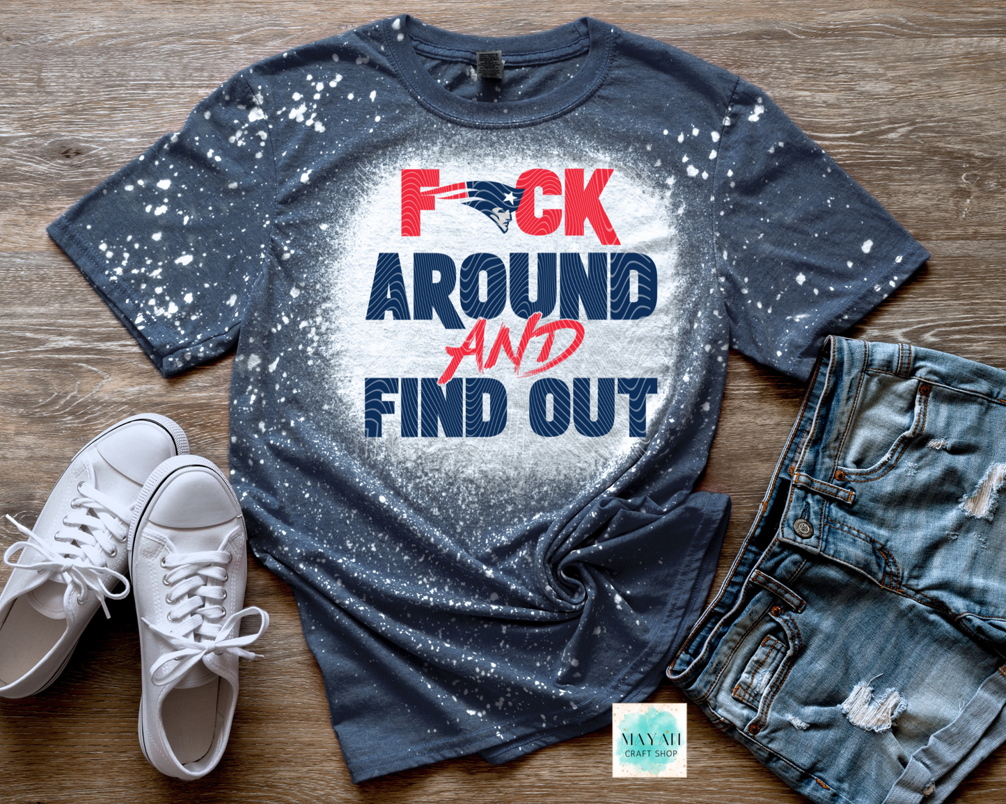 Blue t-shirt with graphic text, white sneakers, and jeans on a wooden surface