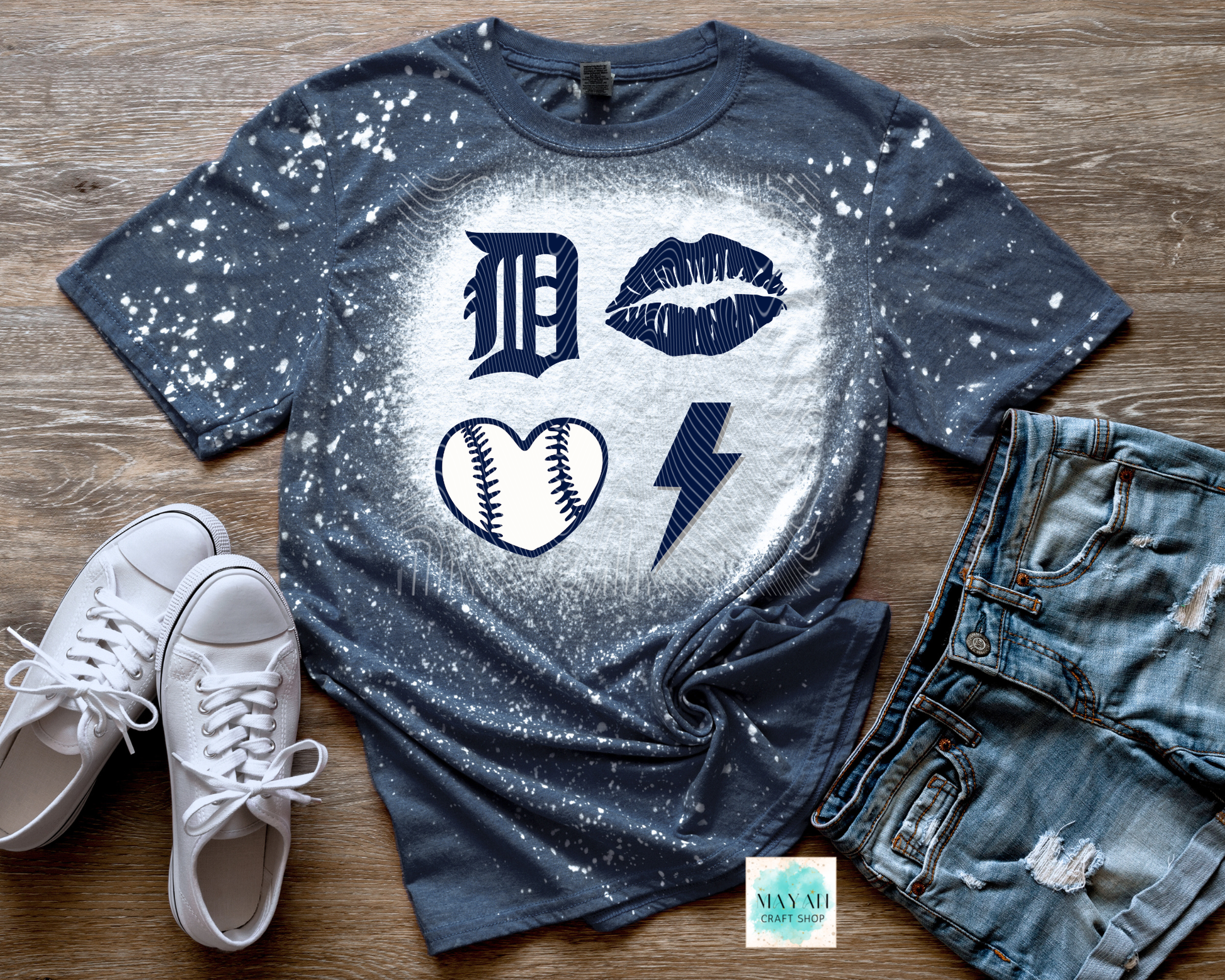 Blue t-shirt with graphic designs on a wooden surface with white sneakers and denim shorts.