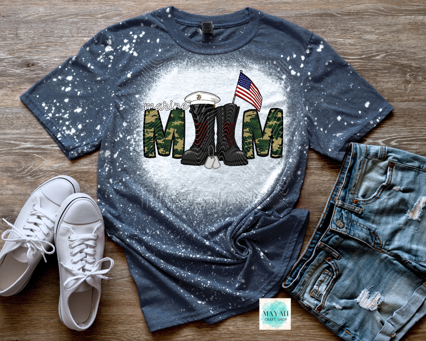 Blue t-shirt with military-themed design on a wooden surface with white sneakers and jeans.