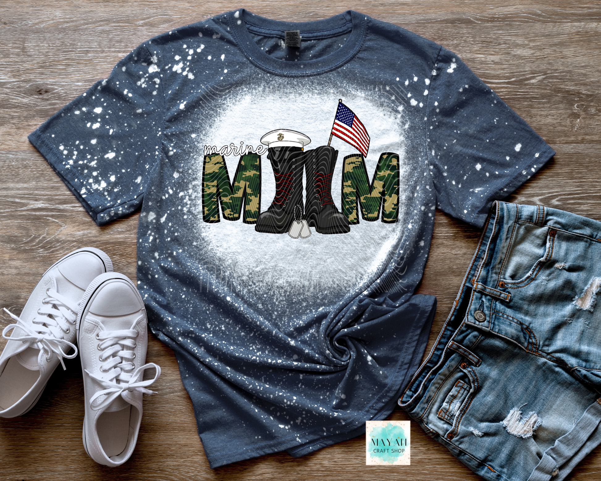 Blue t-shirt with military-themed design on a wooden surface with white sneakers and jeans.