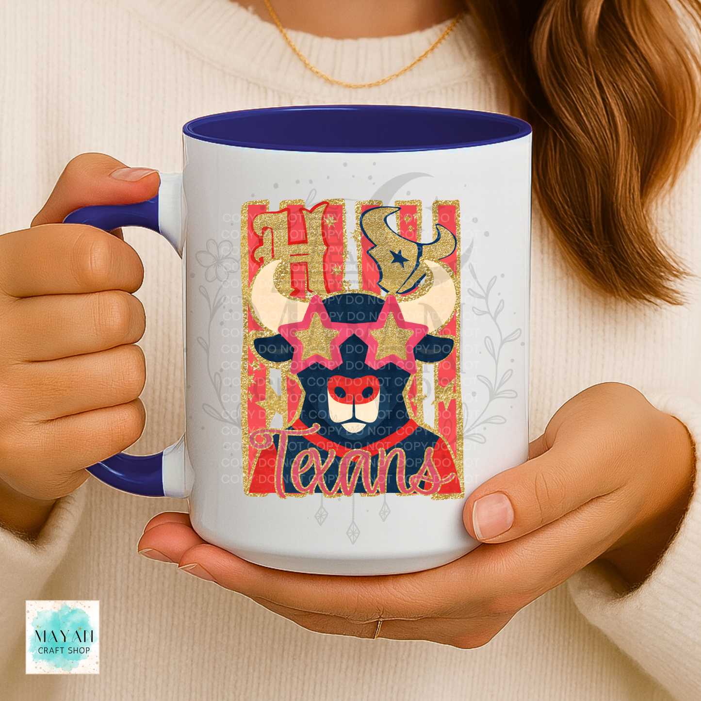 A person holding a white ceramic mug with a blue interior and handle. The mug features a colorful graphic of a stylized Texas bull with words in gold and red.