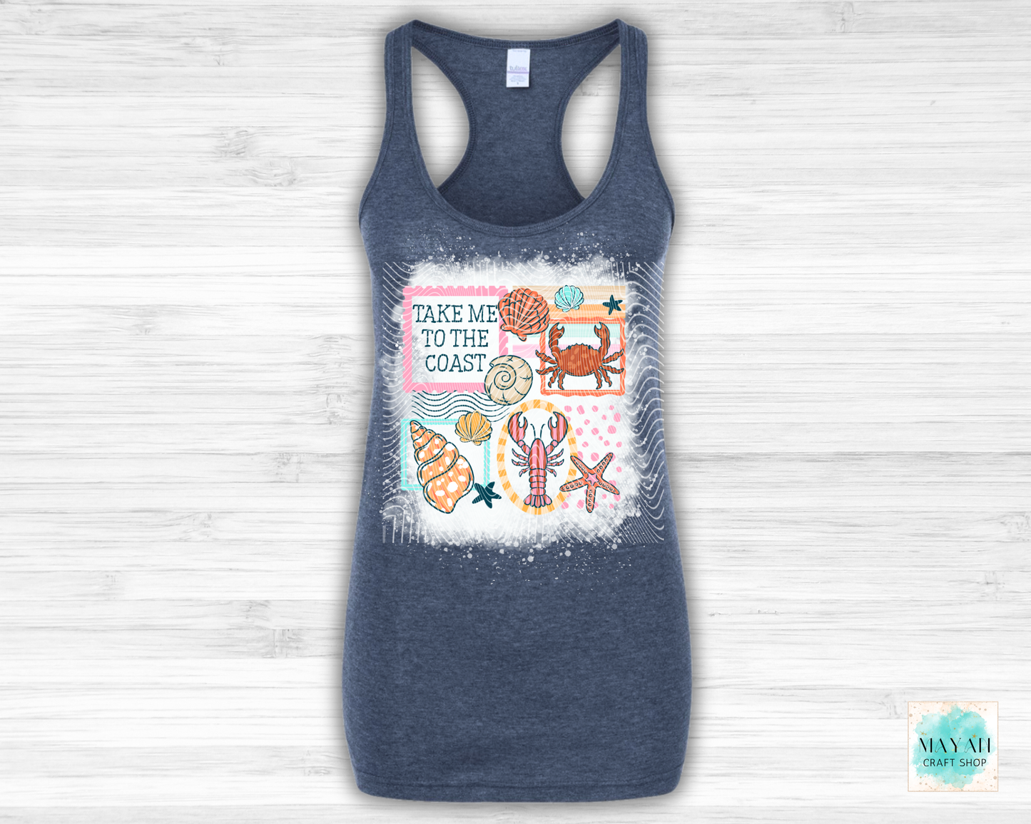 Navy blue tank top with coastal design and text 'Take Me to the Coast' on a light wooden background.