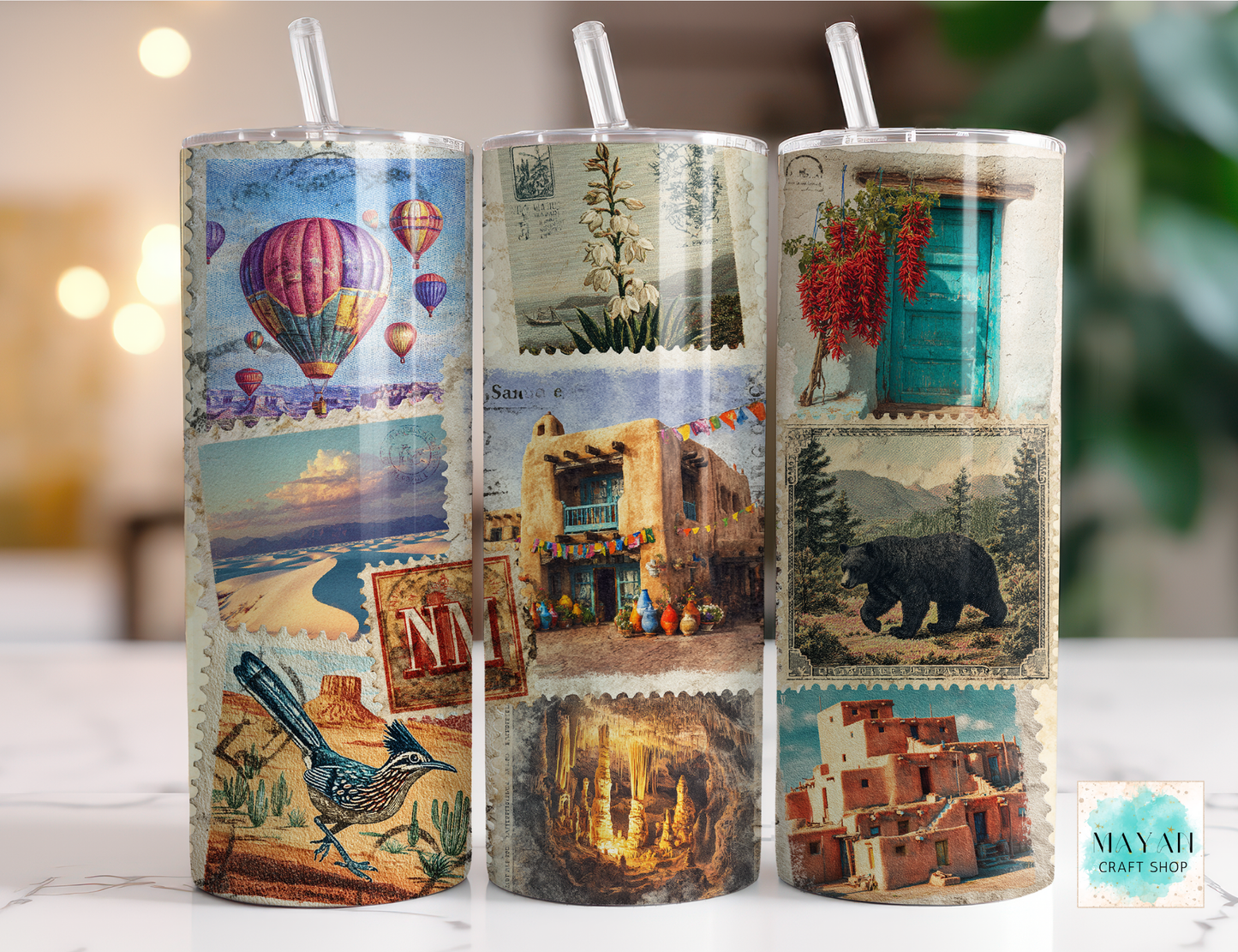 Three cylindrical tumblers with scenic designs on a blurred background