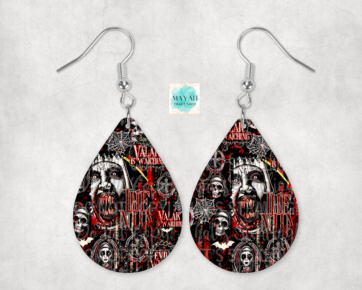 A pair of teardrop-shaped dangle earrings with silver fishhook wires, featuring a black, red, and white collage design with skulls, faces, and gothic text. 