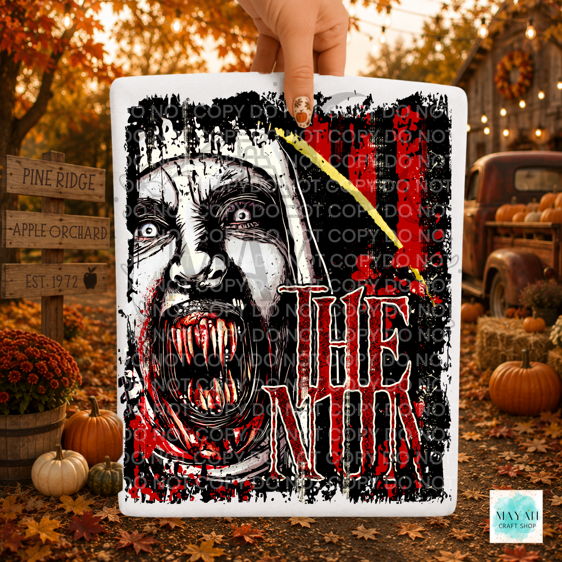 A hand holds a square white sign featuring a horror-style illustration of a screaming woman's face with red blood-like details. The background is a fall yard scene with pumpkins, autumn leaves, and a rustic truck.