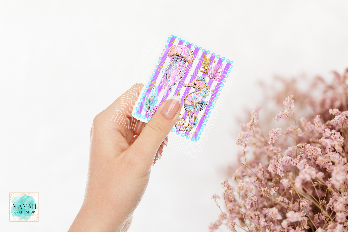 Hand holding a colorful sticker with a seahorse design against a white background with pink flowers.